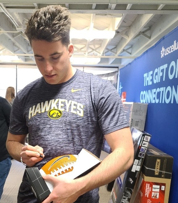 Cade McNamara signs football during UScellular Gift of Connection event