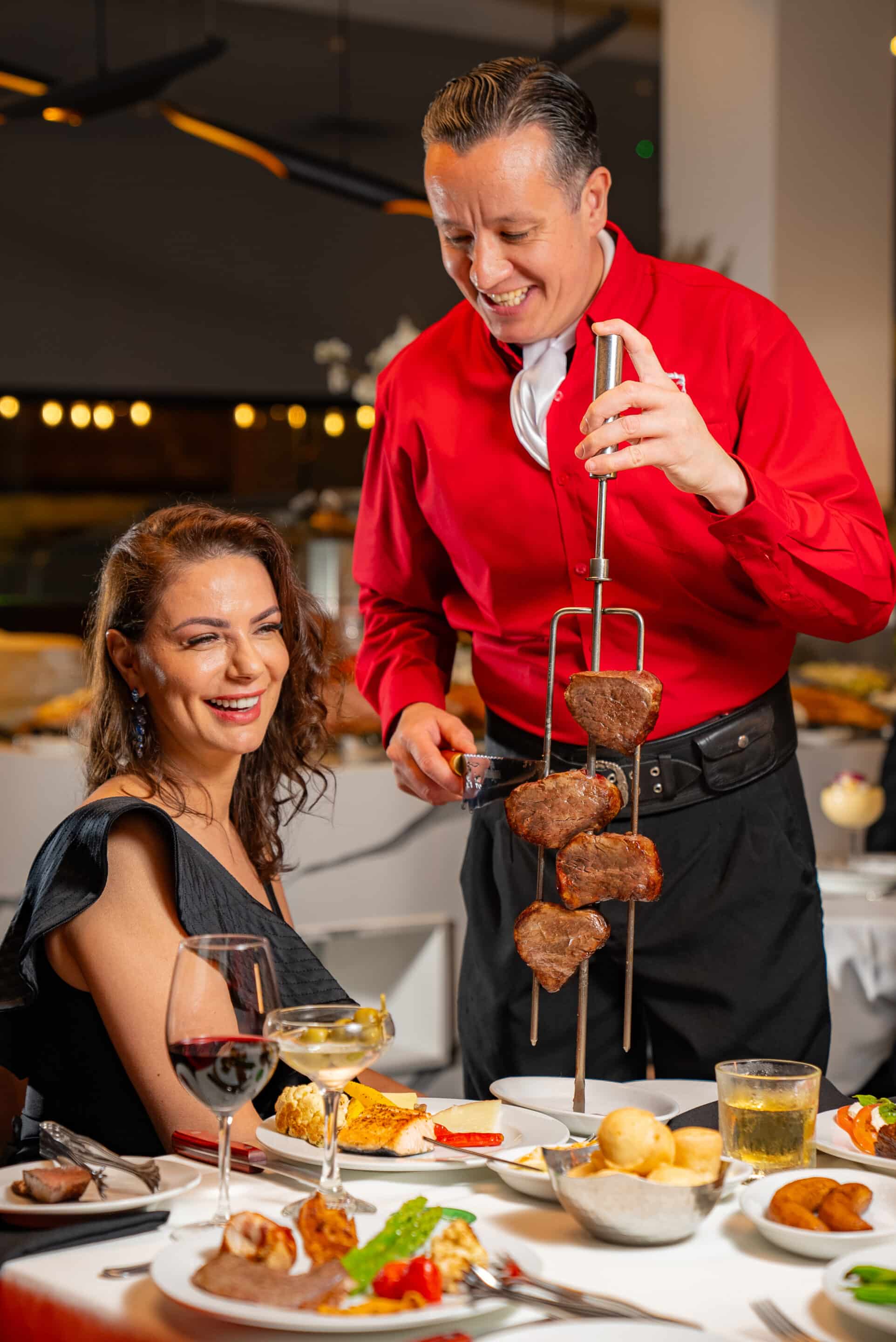Female guest seated at Terra Gaucha being served meat from skewer from server in red