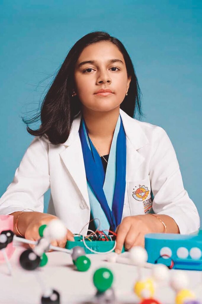 Gitanjali Rao wearing lab coat and medals sitting at desk posing for TIME Magazine's 2020 Kid of the Year award
