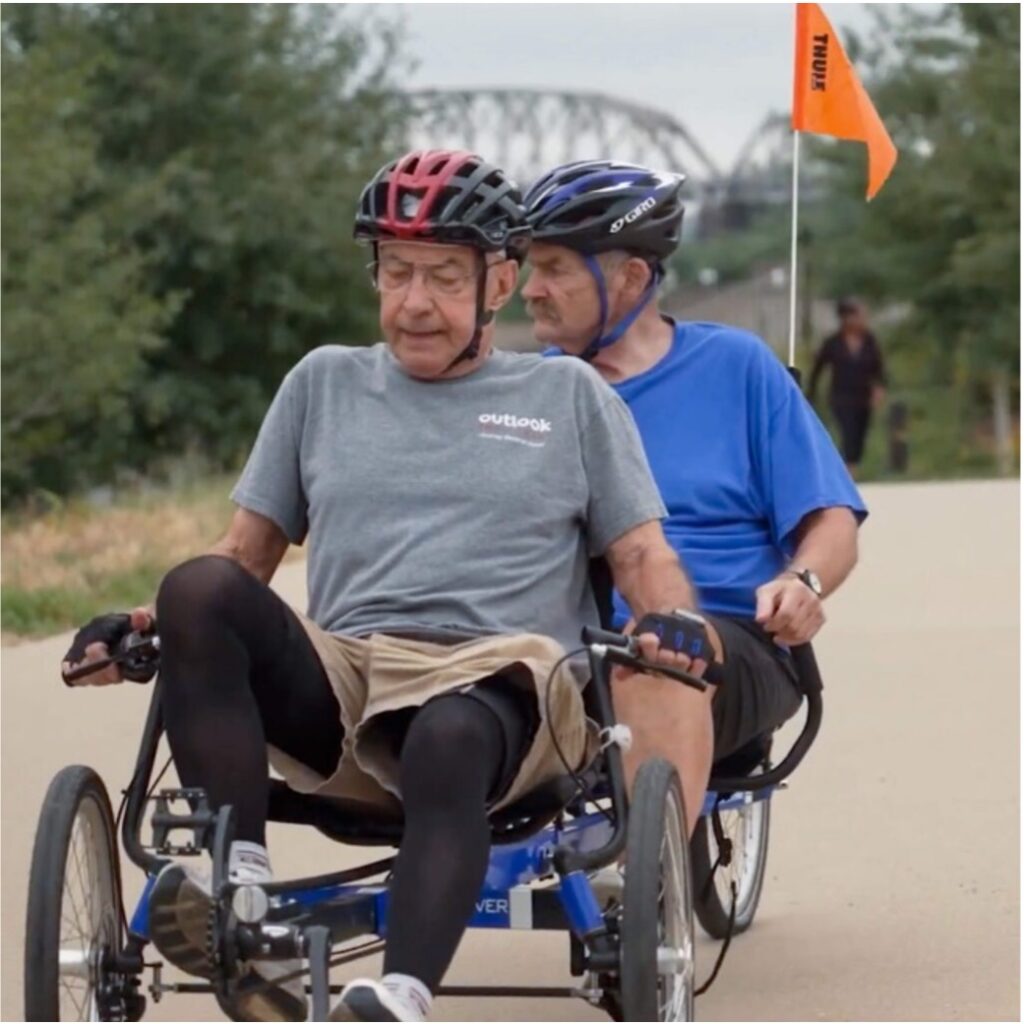 Two men racing on tandem bicycle outdoors for Outlook Enrichment adaptive events