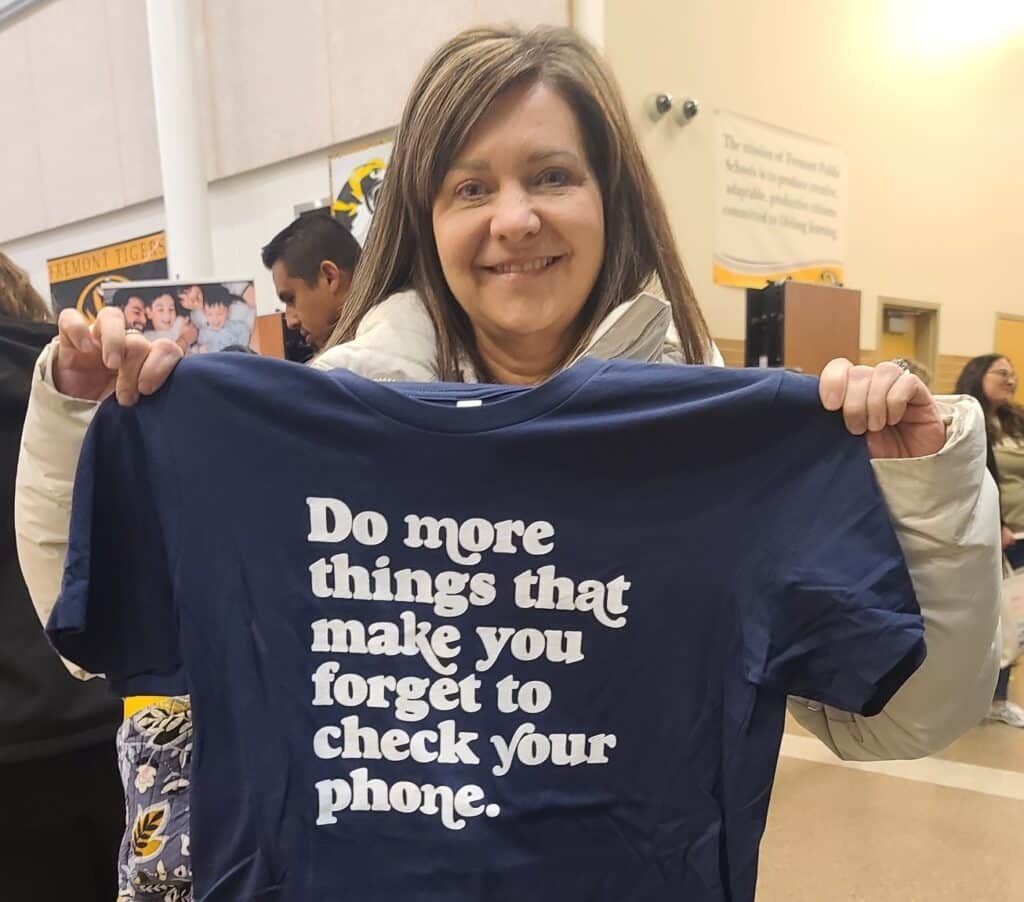 Parent holds up navy tshirt that says "DO more things that make you forget to check your phone" during Screen Sanity Parent Night for UScellular's Global Day of Unplugging campaign