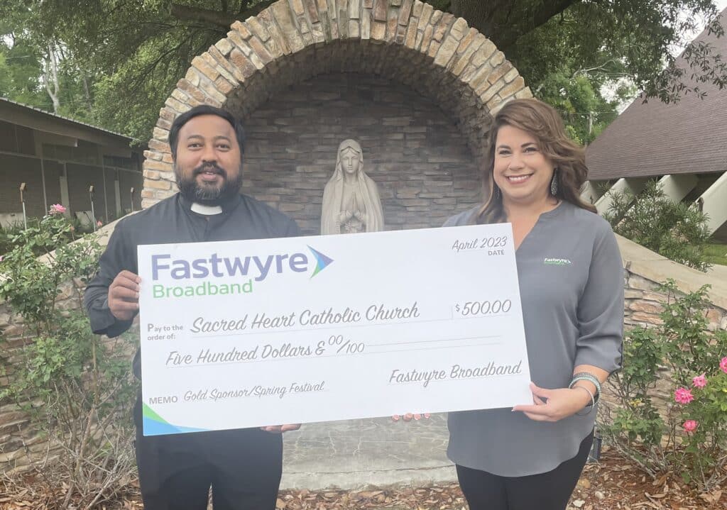 Fastwyre Broadband representative presents a $500 donation check to Sacred Heart Catholic Church during a spring festival sponsorship.