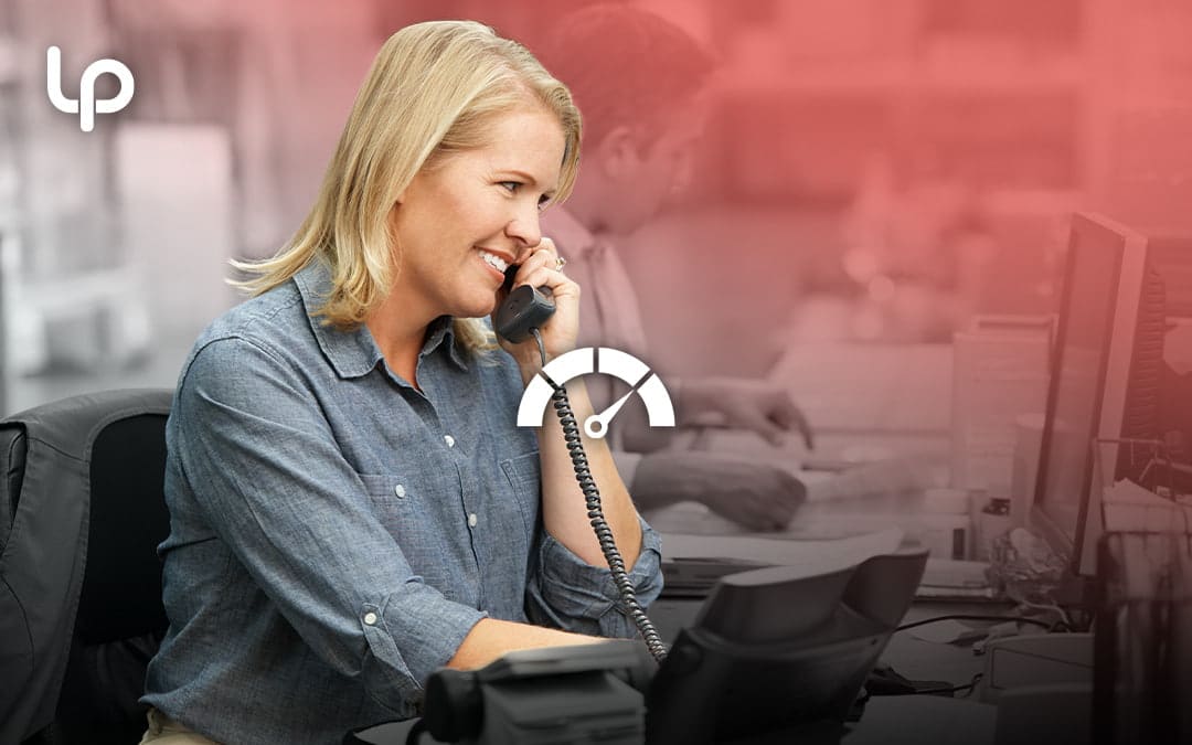A smiling woman talks on a corded office phone at her desk